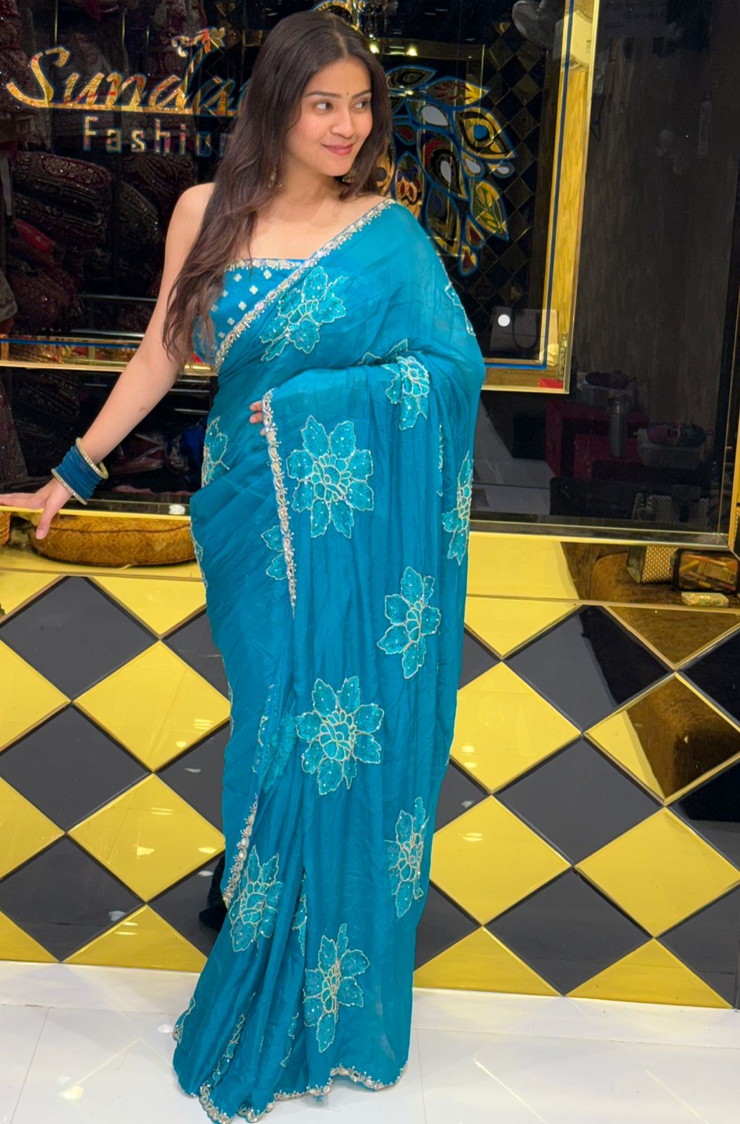 Woman wearing a blue saree with floral patterns in a store setting.